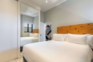 A bedroom with a large bed, a wooden headboard, and a mirror reflecting the room. - Views, Fireplace, Sea Point - Mnt Nelson Townhouse (Cape Town)