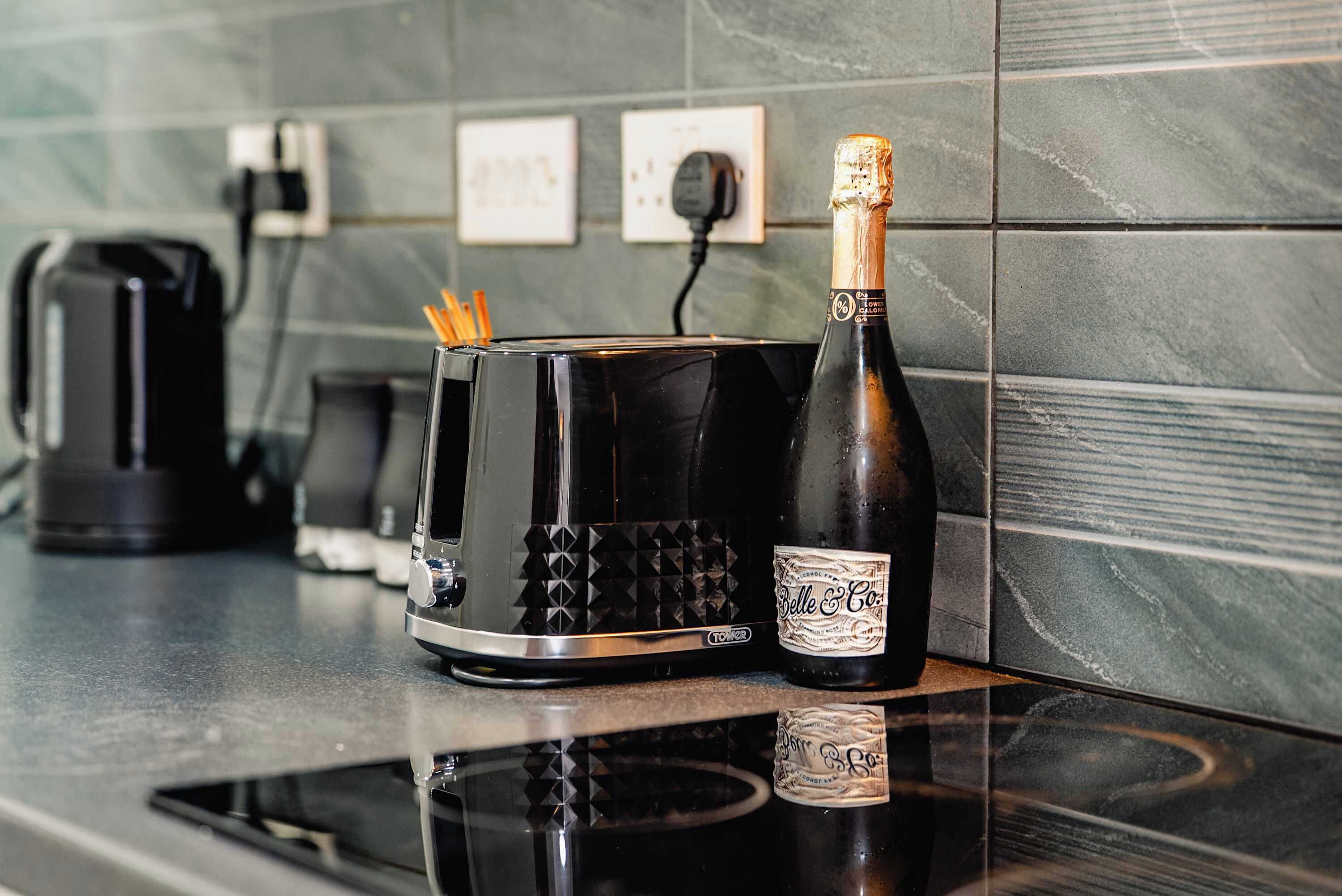 A kitchen counter with a black toaster, a bottle of Belle & Co champagne, and a coffee maker.