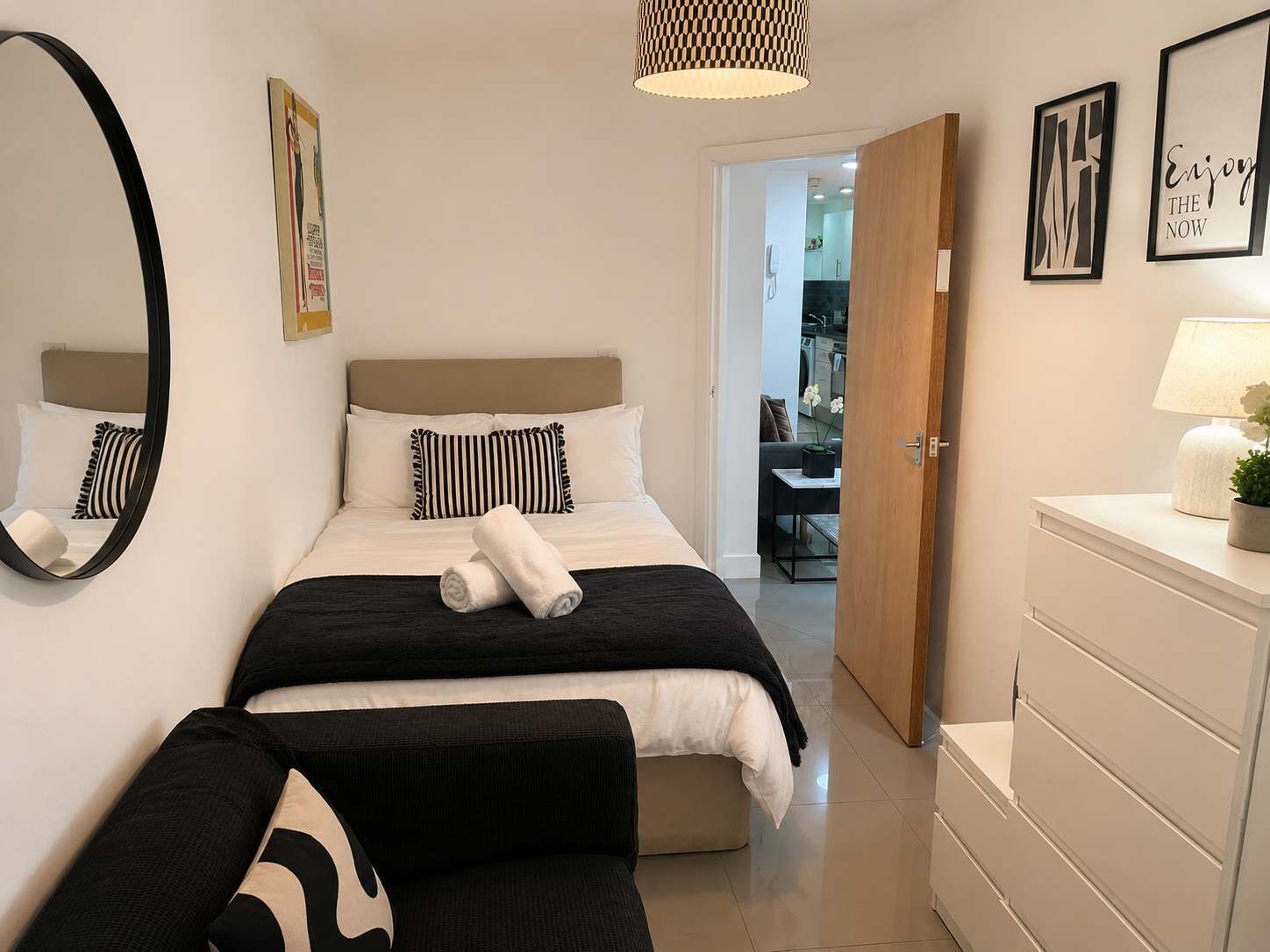 A hotel room with a bed, a bedside table with a lamp, a mirror, and a door leading to a bathroom.