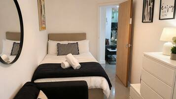 A hotel room with a bed, a bedside table with a lamp, a mirror, and a door leading to a bathroom.