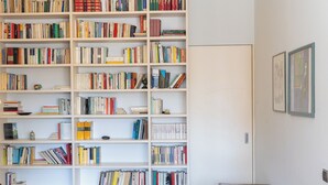 Een grote, witte boekenkast vol boeken en dvd's, een houten tafel en twee ingelijste foto's aan de muur.
