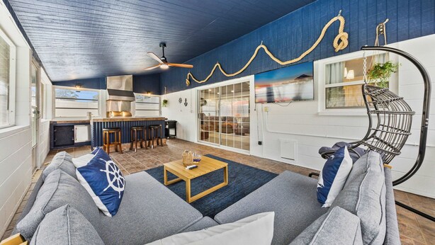 Een moderne woonkamer met een grijze bank, een houten salontafel en een plafondventilator.