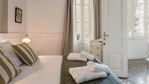 A hotel room with a bed, a bedside lamp, a dresser, and a door leading to a balcony. - Spacious 5-bedroom apartment in charming Barcelona with AC (Barcelona)