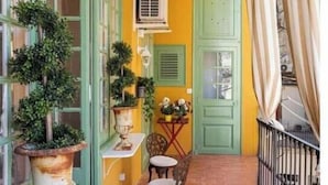 A balcony with a tiled floor, a table with chairs, potted plants, and a door with a green shutter. - Spacious 5-bedroom apartment in charming Barcelona with AC (Barcelona)