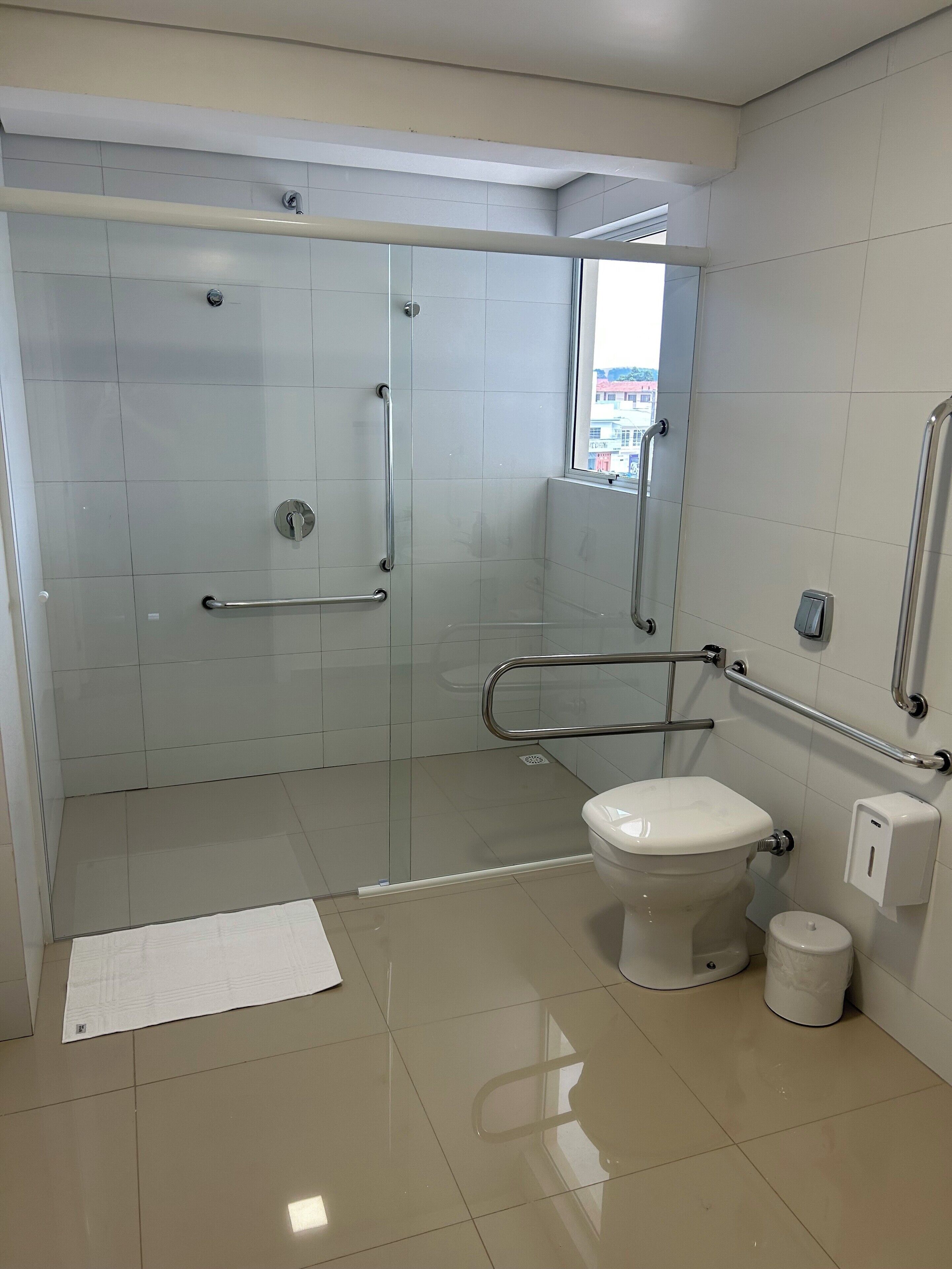A modern bathroom with a glass-enclosed shower, a toilet, and a hand sanitizer dispenser.