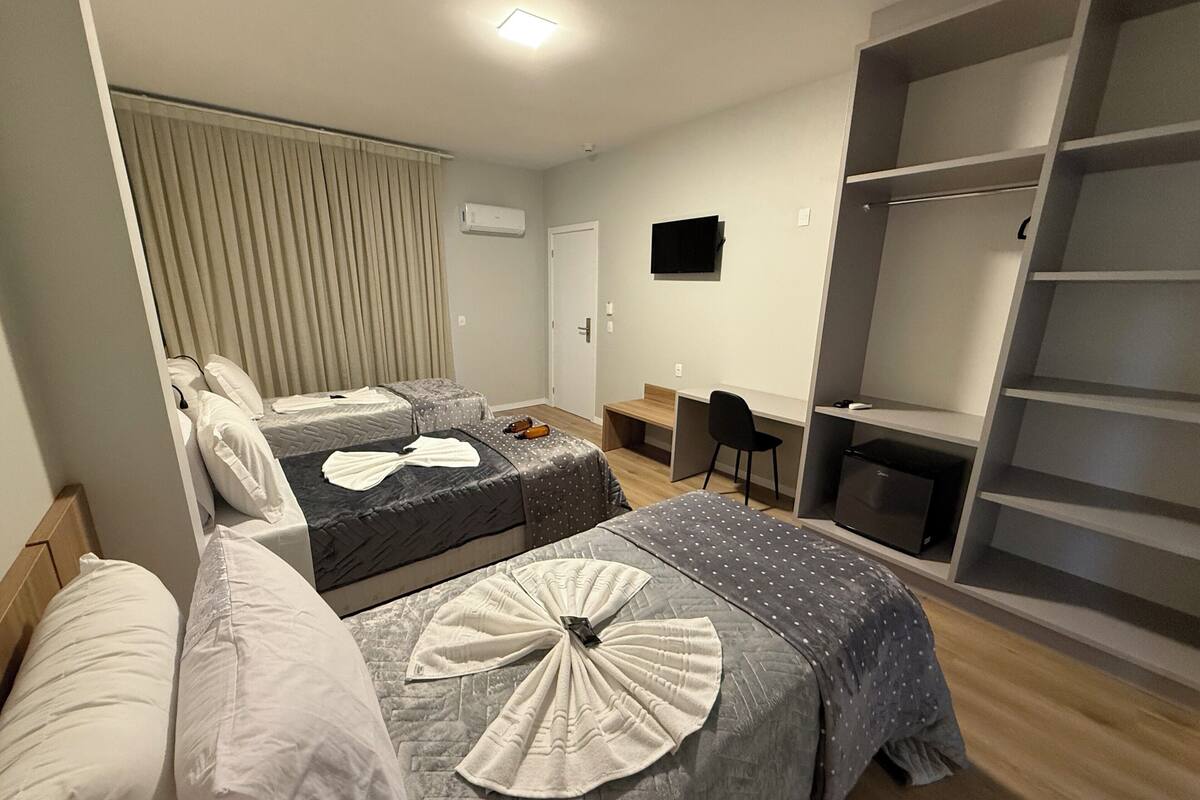 A hotel room with two beds, a desk, a chair, a TV, and a wardrobe.