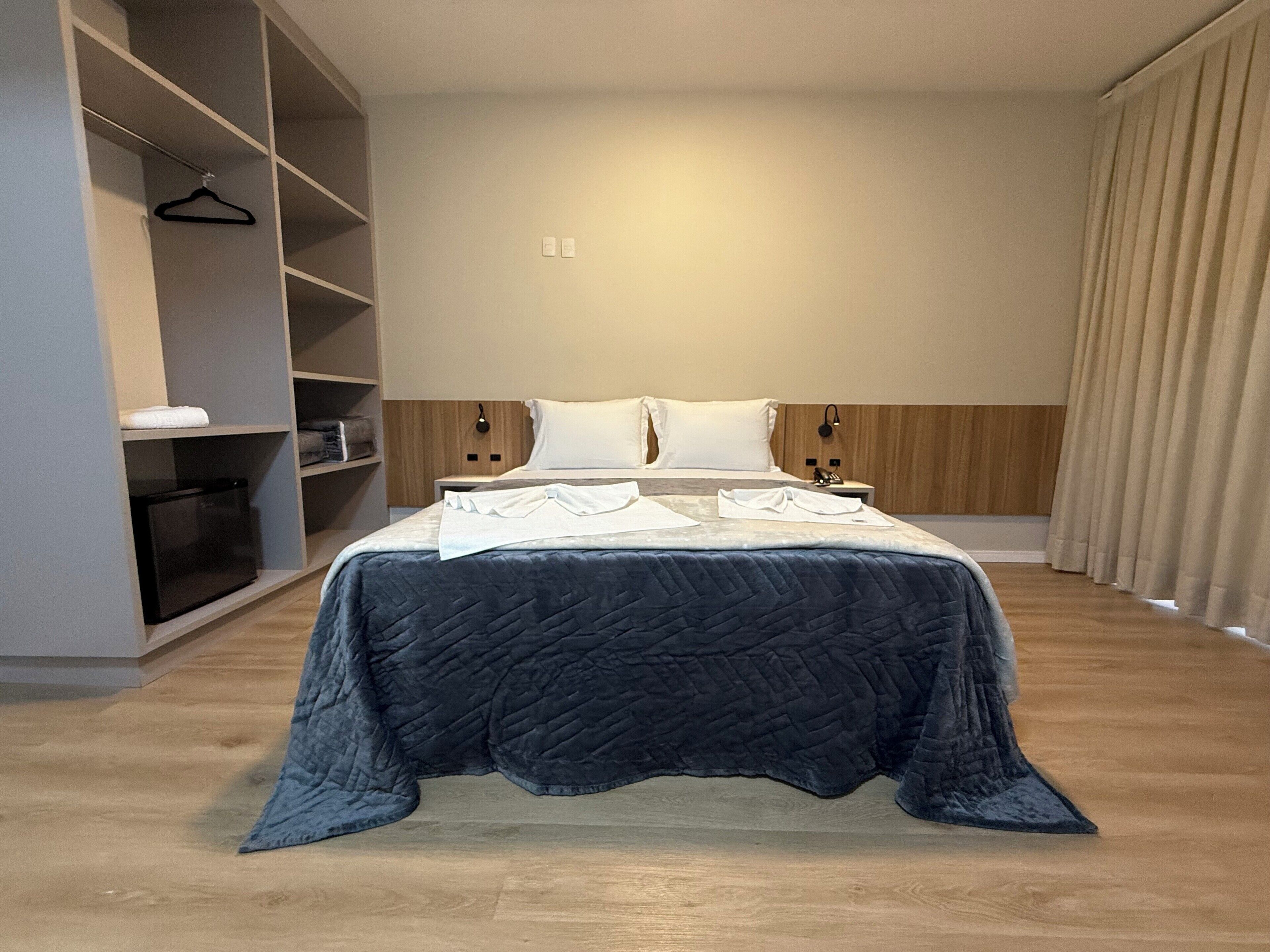 Una habitación de hotel moderna con una cama grande, un armario y una mesita de noche.