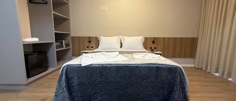 Una habitación de hotel moderna con una cama grande, un armario y una mesita de noche.