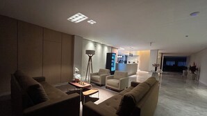 A modern living room with a sofa, armchairs, a coffee table, and a floor lamp. There is a kitchen area in the background. - Bon Vivant Hotel (Fraiburgo)
