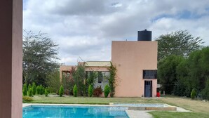 A swimming pool with a wooden deck in the foreground, a modern building with a flat roof in the background, and a clear sky. - Olturoto Pumzika (Olturoto)