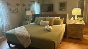 Un dormitorio ordenado con cama, almohadas, mesita de noche, lámpara y espejo.