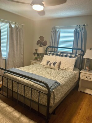 A bedroom with a bed, a nightstand, a lamp, a ceiling fan, and a window with curtains.