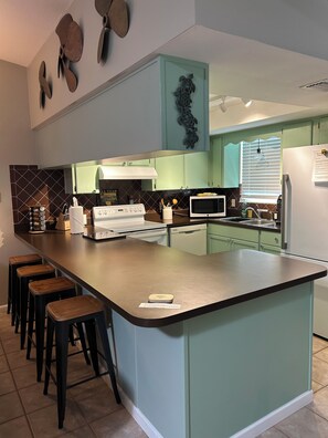 A modern kitchen with a central island, bar stools, a microwave, and a refrigerator. - Natures Nest
Waterfront (Homosassa)