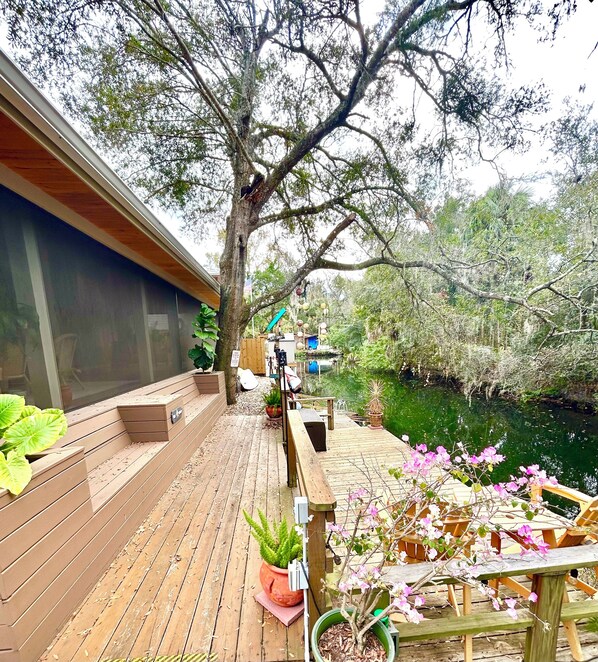 A wooden deck with seating, a potted plant, and a view of a water body.