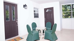 A room with a dark brown door, a white wall, a small window, a round table with four chairs, and a doormat. - Peaceful Island Retreat w/ Private Patio + Parking (Leeward Settlement)