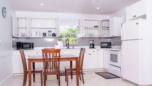 A modern kitchen with white cabinets, a dining table with chairs, a microwave, a coffee maker, and an oven. - Peaceful Island Retreat w/ Private Patio + Parking (Leeward Settlement)