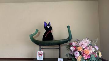 Una statuina di un gatto nero su una poltrona verde, un cartello di divieto di fumare e un bouquet di fiori su un tavolo.