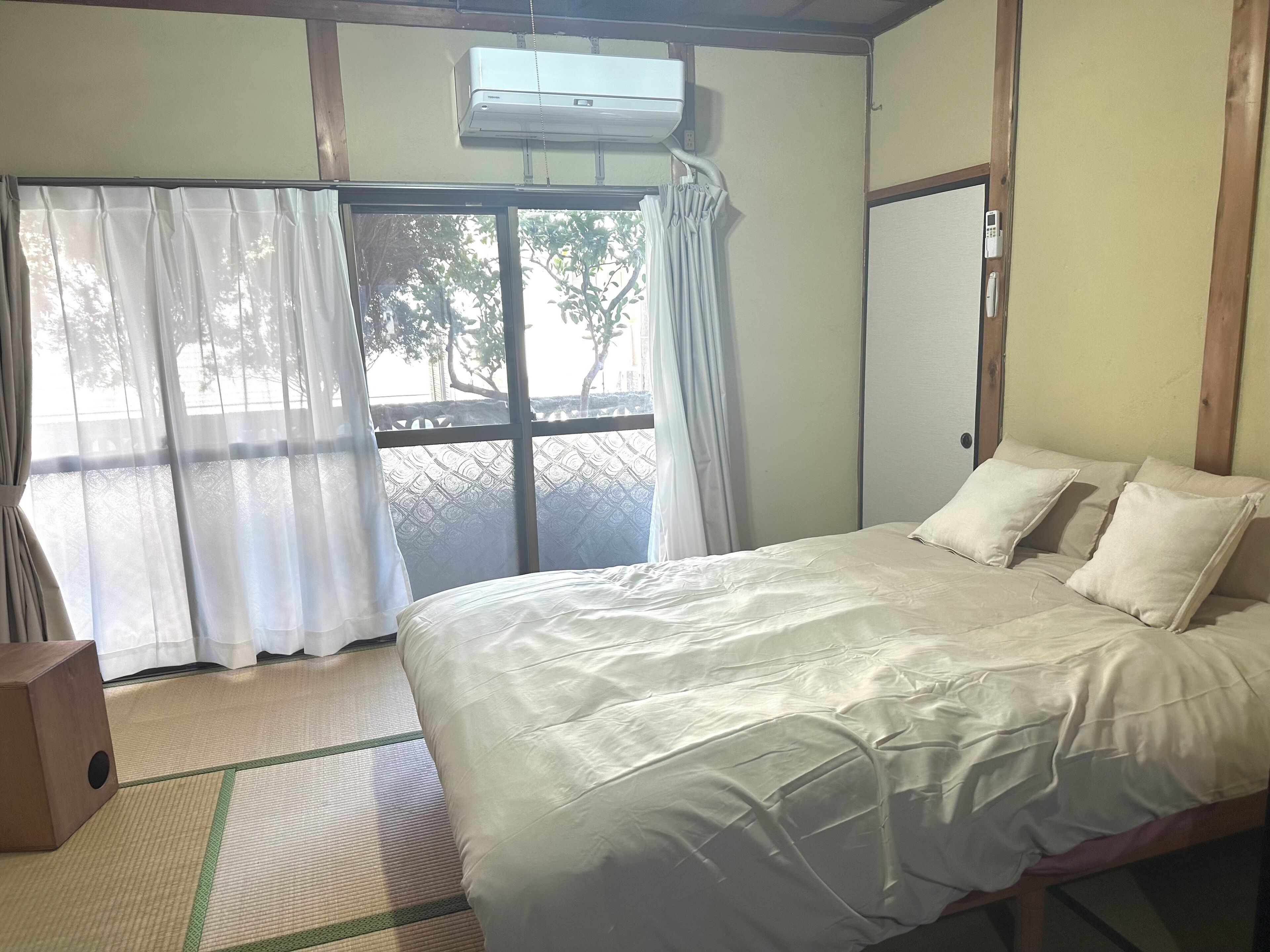 Una habitación con una cama, una puerta corrediza de vidrio, un equipo de aire acondicionado y piso de madera.