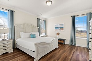 A bedroom with a large bed, a nightstand, a dresser, and a window with curtains. - Beach House - C Shucker by PHG (Mexico Beach)