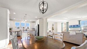 A spacious kitchen with white cabinets, a dining table with chairs, and a chandelier. - Beach House - C Shucker by PHG (Mexico Beach)
