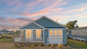 A single-story house with a porch, a small garden, and a clear sky. - Beach House - C Shucker by PHG (Mexico Beach)