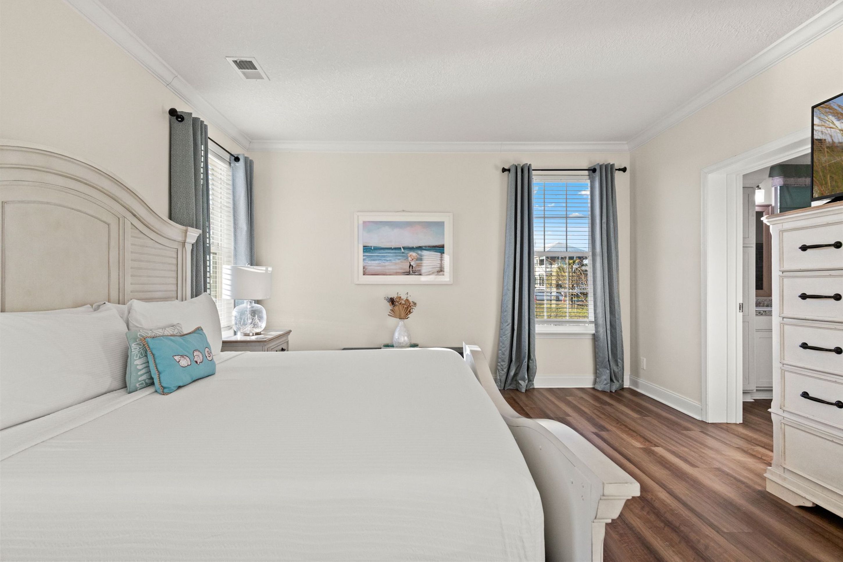 Une chambre à coucher avec un grand lit, une table de chevet avec une lampe, une commode et une fenêtre avec des rideaux.