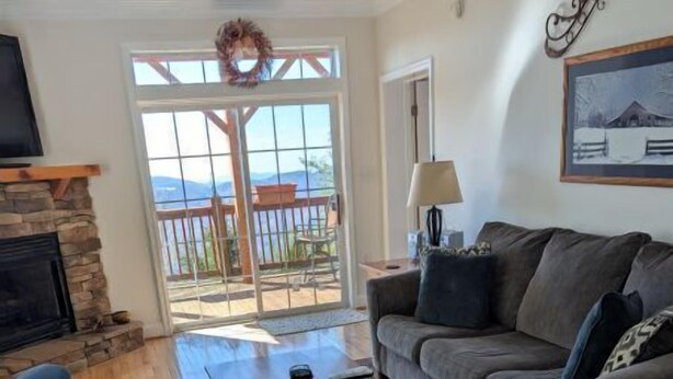 A living room with a stone fireplace, a wooden coffee table, a sofa, and a view through a glass door to an outdoor deck. - KLTD1  Klonteska Manor  An unforgettable mountain getaway! (Beech Mountain)