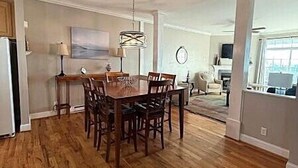 A spacious dining area with a wooden table and chairs, a chandelier, and a view of the living room in the background. - KLTA6  Beach to Beech Villa  2 BR/2 BA Condo Walking distance to Town (Beech Mountain)