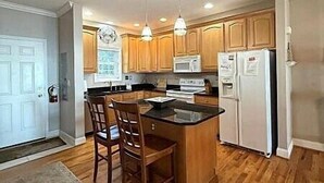 A modern kitchen with wooden cabinets, a central island with bar stools, a microwave, and a refrigerator. - KLTA6  Beach to Beech Villa  2 BR/2 BA Condo Walking distance to Town (Beech Mountain)