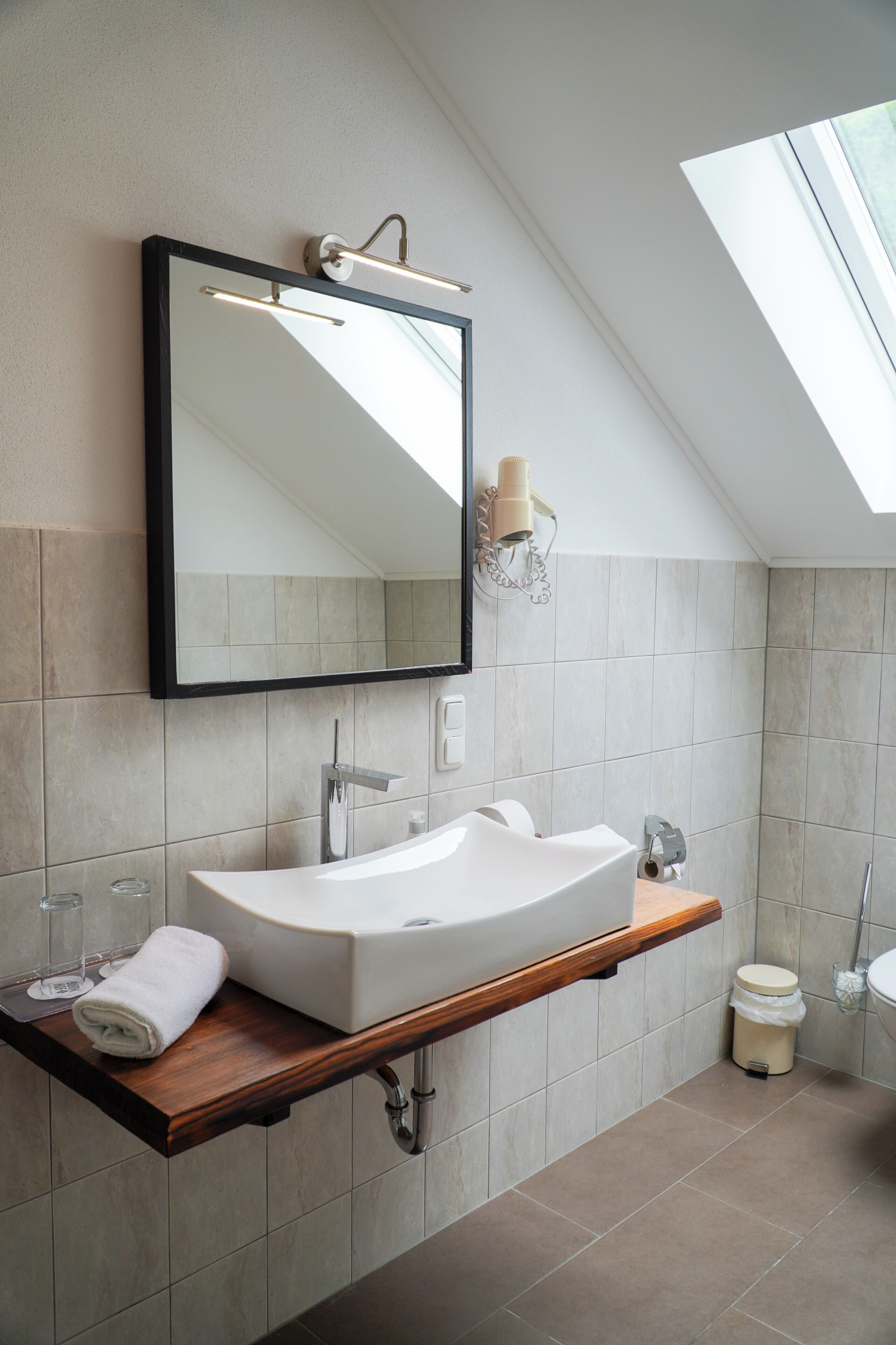Een moderne badkamer met een vrijstaand wastafelmeubel, een grote spiegel en een dakraam.