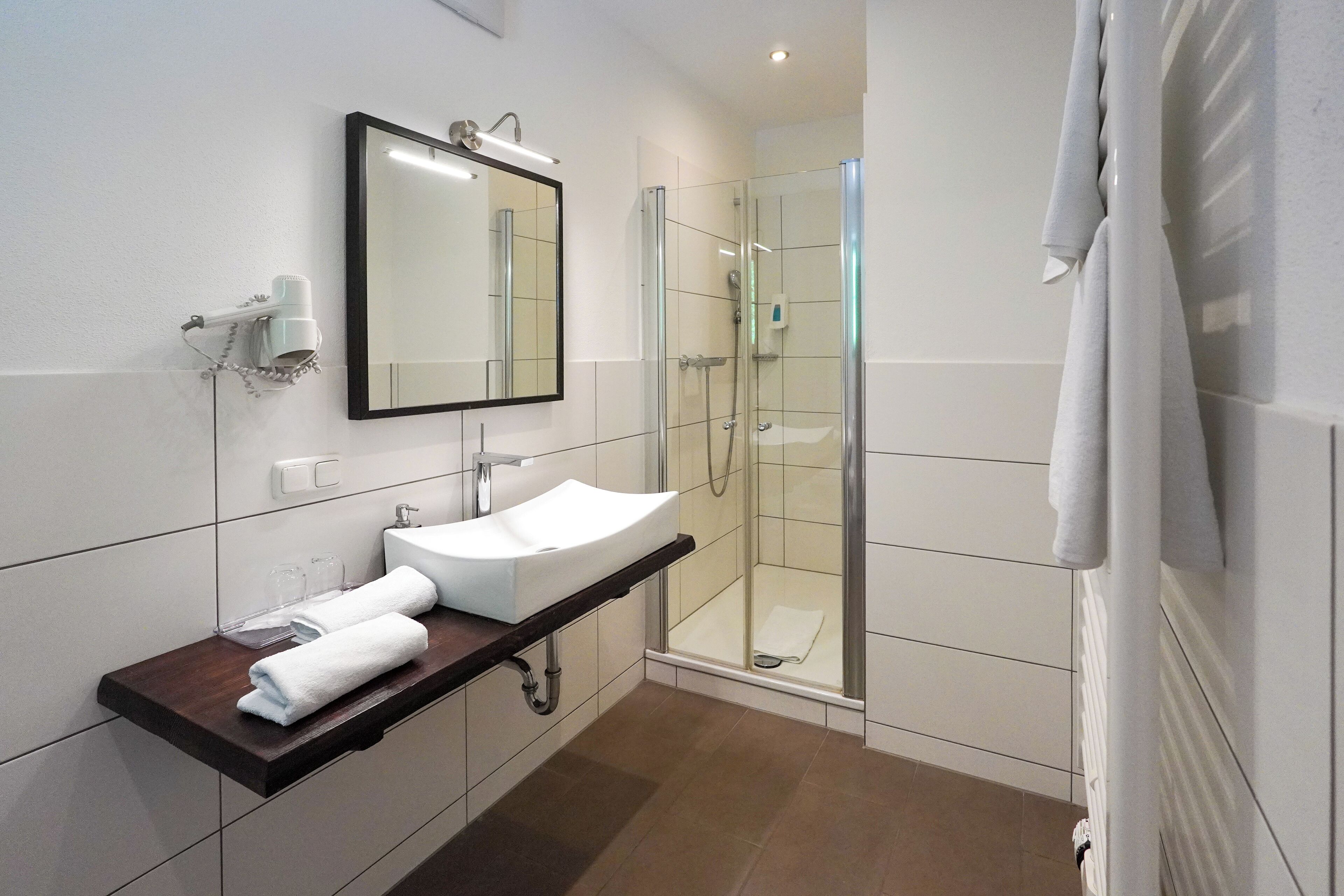 Een moderne badkamer met een wit wastafelmeubel, een spiegel, een douche met glazen wanden en een handdoekhouder.