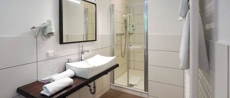 Un baño moderno con lavamanos blanco, espejo, ducha con mampara de cristal y un perchero para toallas.