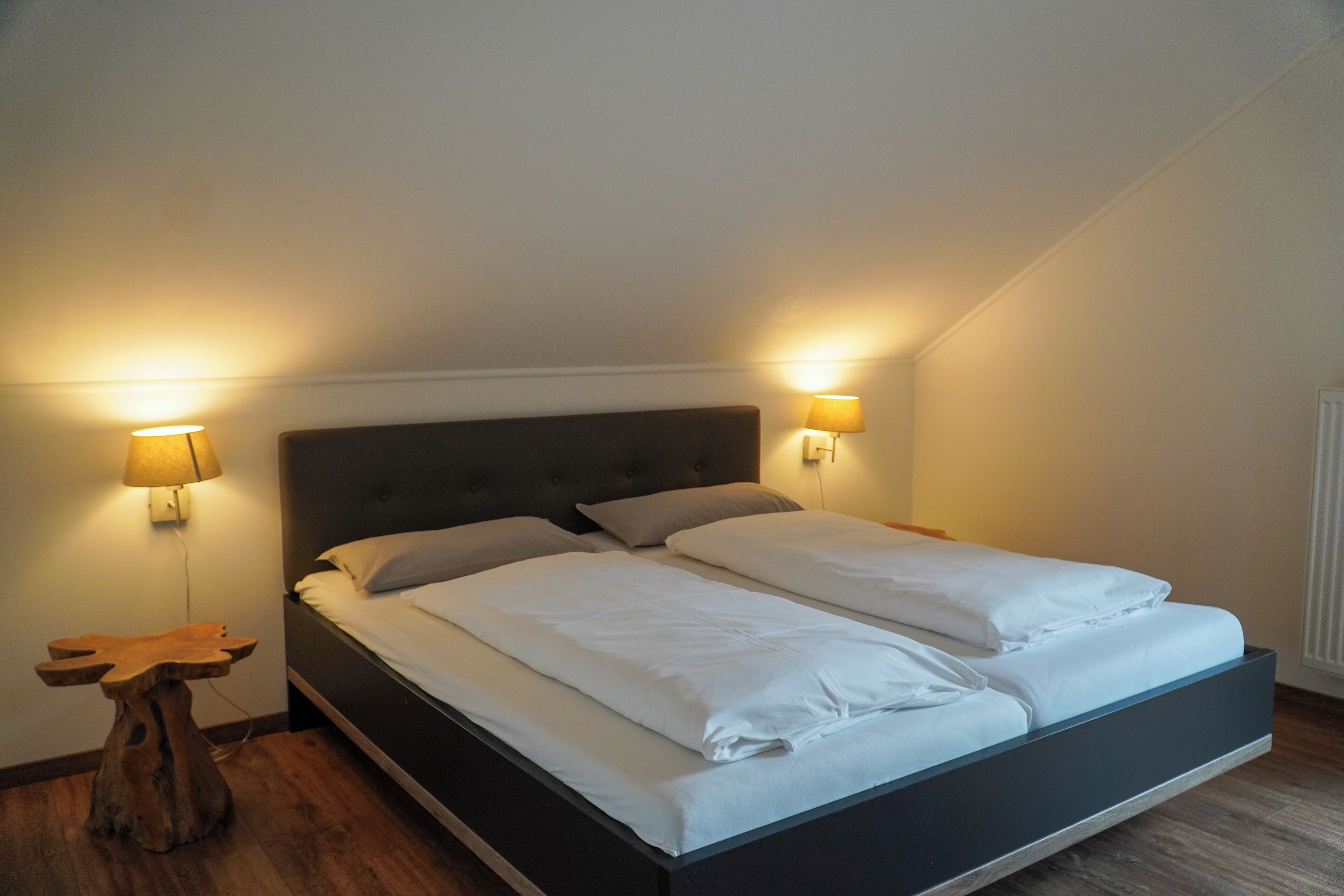 A bedroom with a large bed, two bedside lamps, and a wooden nightstand.