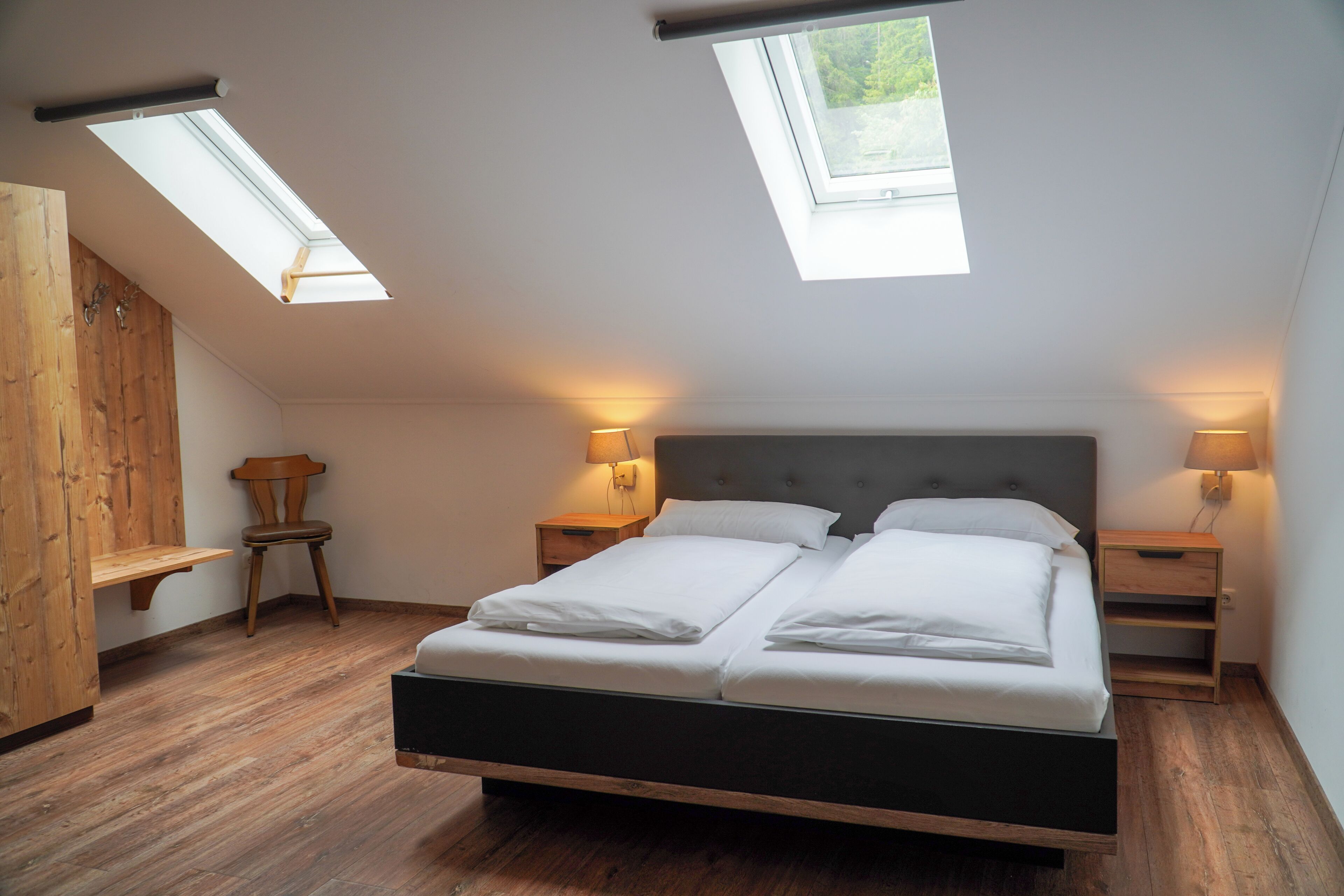 Un dormitorio con una cama grande, tragaluces, suelo de madera y lámparas de noche.