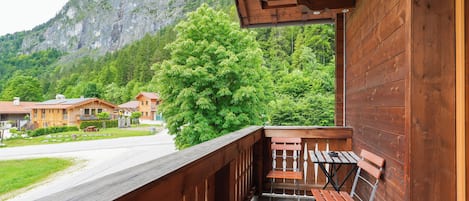 A wooden balcony with a table and chair, overlooking a mountain and a road with buildings.