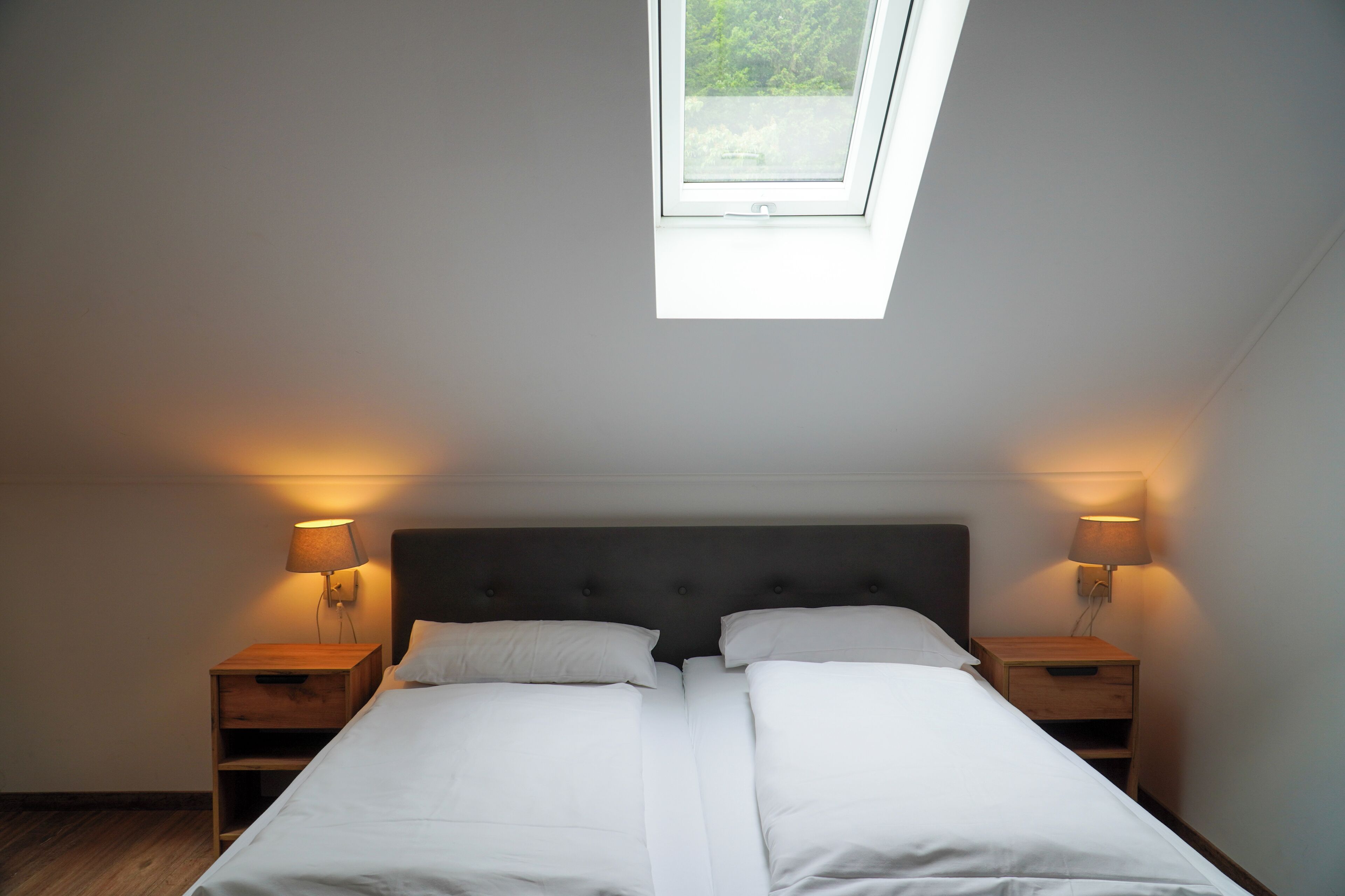 A bedroom with a skylight, two bedside tables with lamps, and a large bed.