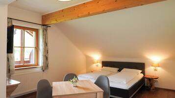 A cozy room with a wooden ceiling, a bed with white bedding, a dining table with chairs, and two bedside lamps.