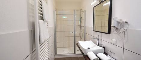 A modern bathroom with a glass-enclosed shower, a white sink, and a mirror.
