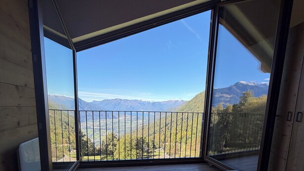 A bedroom with a large window overlooking a mountainous landscape. There are two neatly folded towels on the bed. - Chalet Altea View: panoramic Lake Como, 8 places, garden and barbecue. (Mello)