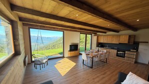 A spacious living area with a wooden ceiling, a dining table set for four, a sofa, and a TV. - Chalet Altea View: panoramic Lake Como, 8 places, garden and barbecue. (Mello)