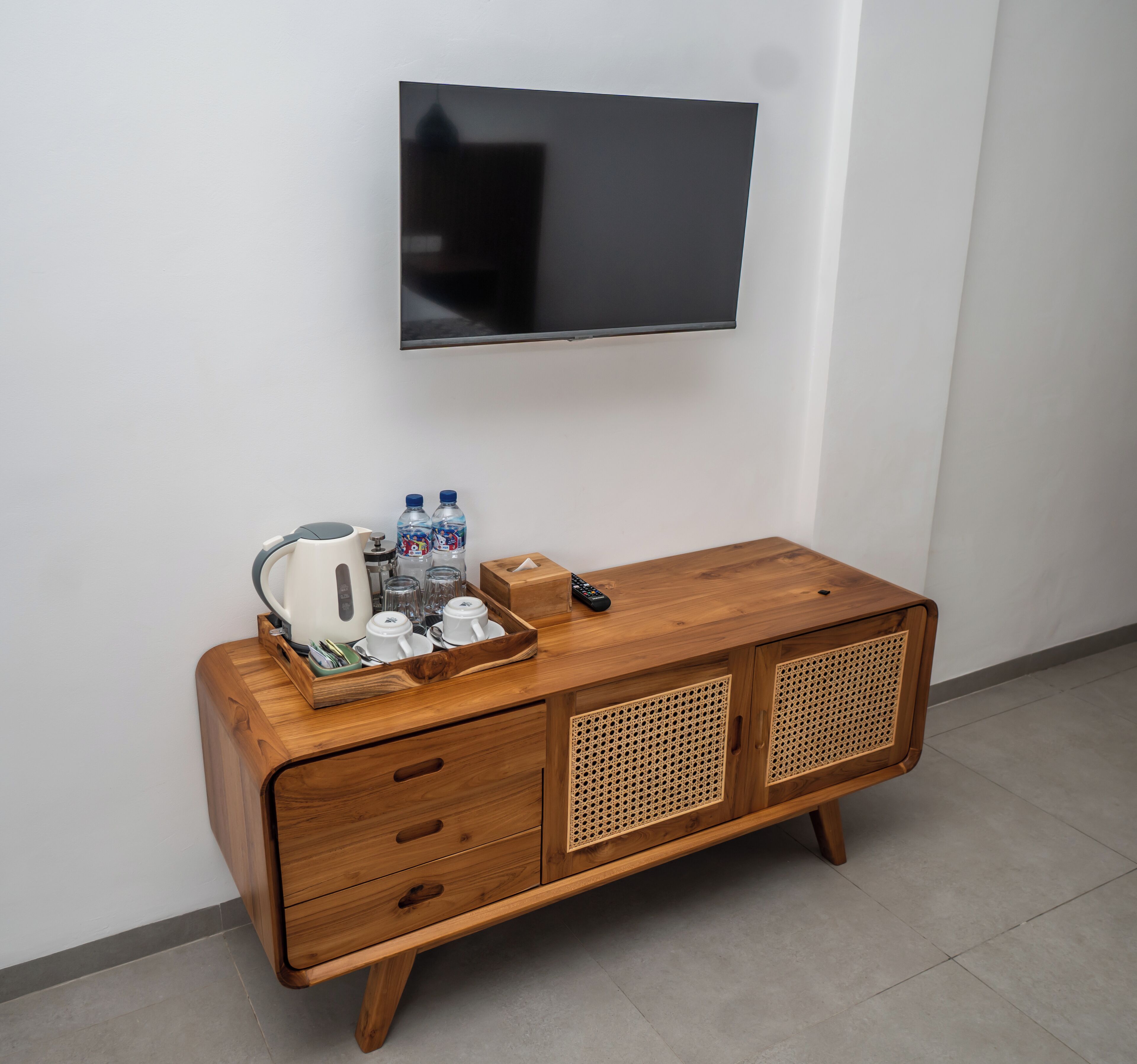 A wooden cabinet with a tray of water bottles, a kettle, and a remote control.