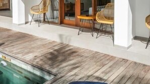 A covered outdoor area with a pool, wooden flooring, and wicker chairs. - Kemari Ubud (Ubud)