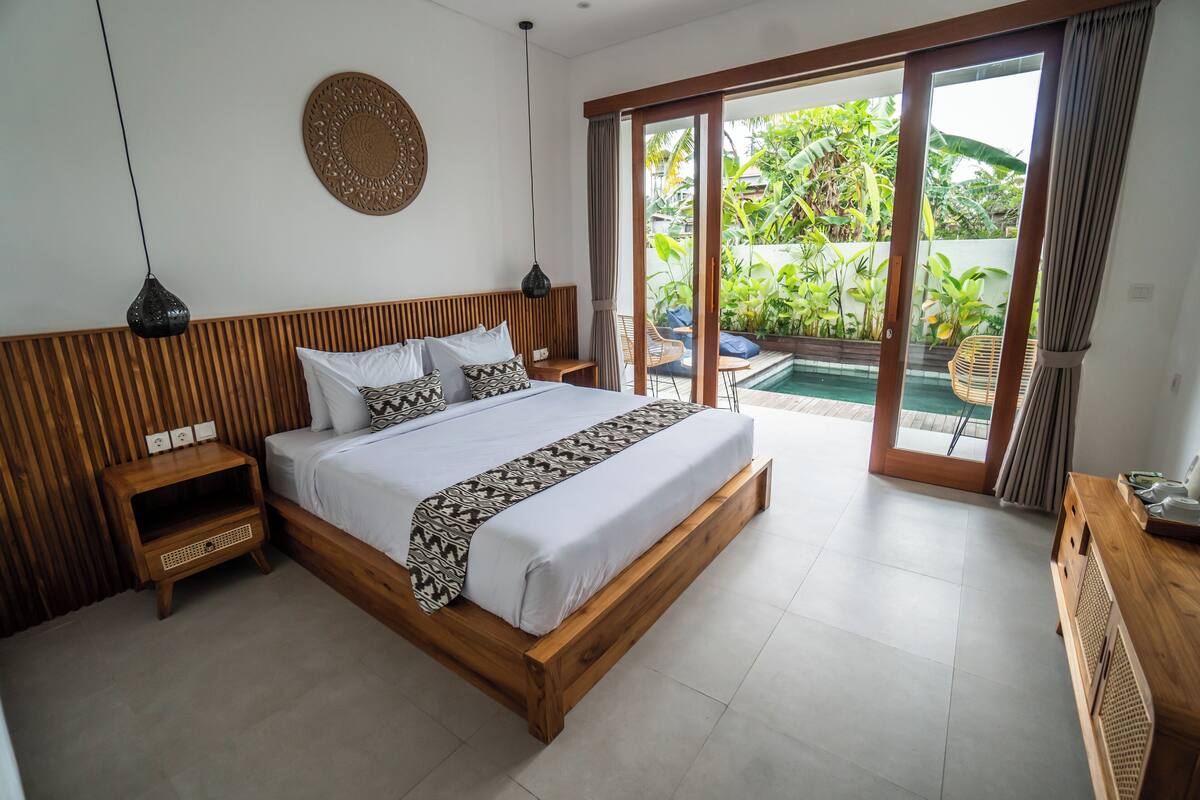 Une chambre dotée d’un grand lit, d’une tête de lit en bois et offrant une vue sur une piscine grâce à une porte-fenêtre coulissante.