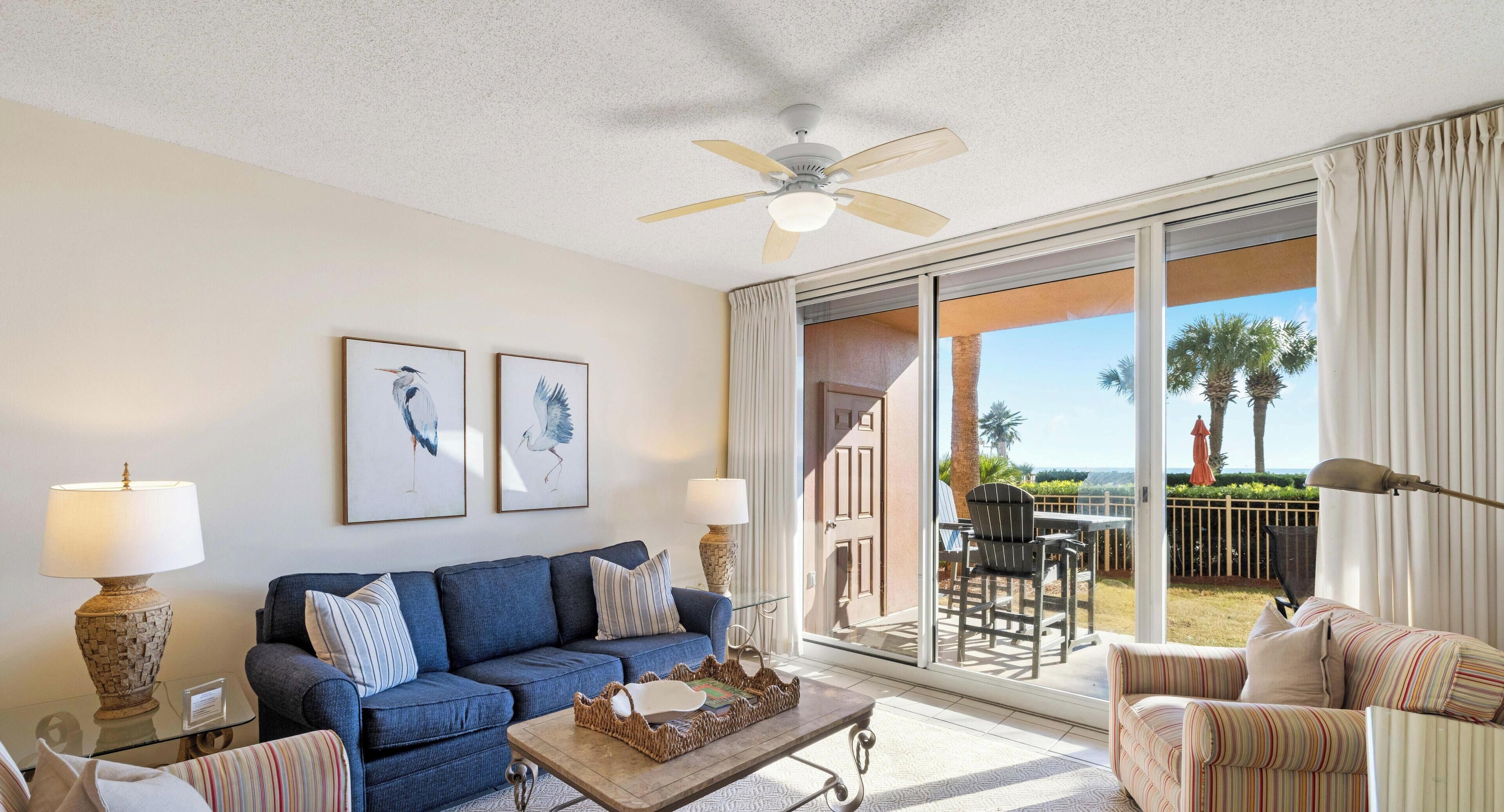 A living room with a blue sofa, a coffee table, and a view of the outdoors through large sliding glass doors.