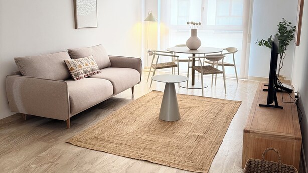 Ein modernes Wohnzimmer mit einem beigen Sofa, einem runden Couchtisch und einem Esstisch mit Stühlen.
