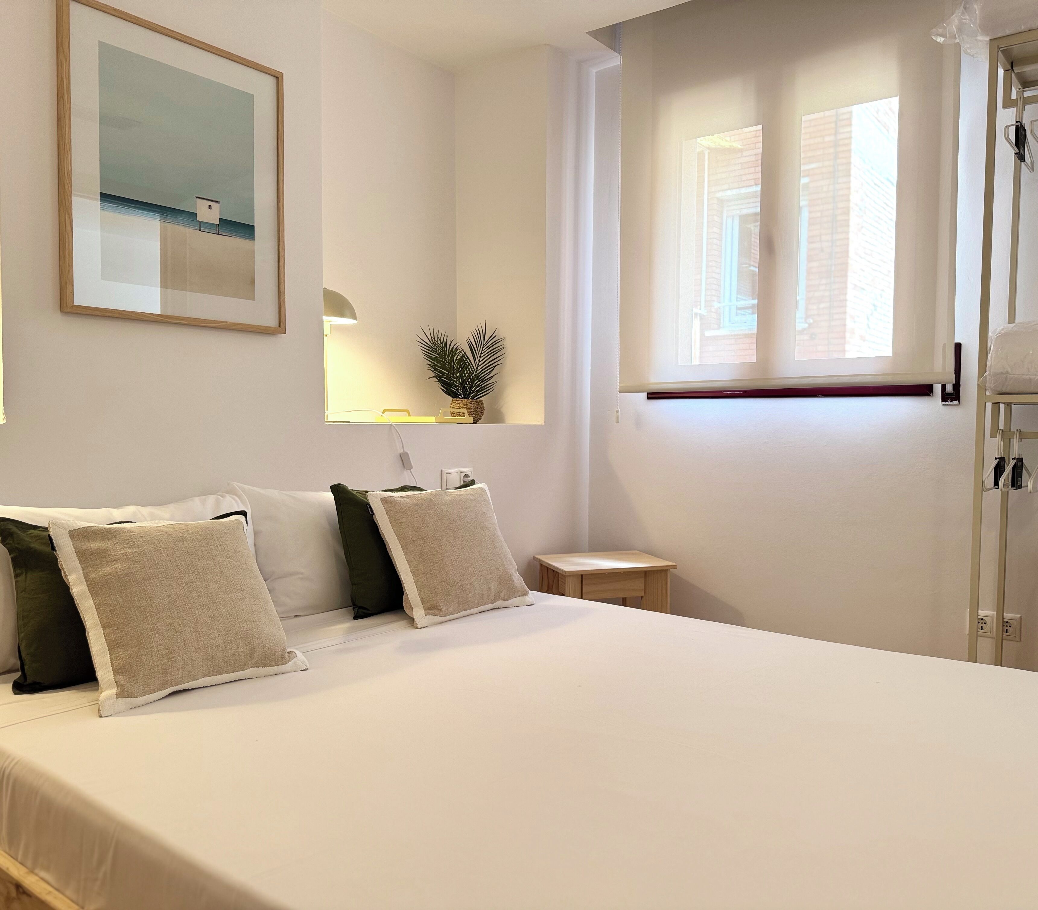 Una camera da letto ordinata con un letto grande, un comodino, una piccola pianta in vaso e una finestra con persiane.
