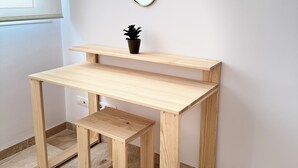 Ein Holztisch mit einem Spiegel darüber, eine kleine Topfpflanze auf dem Tisch und ein Fenster links.