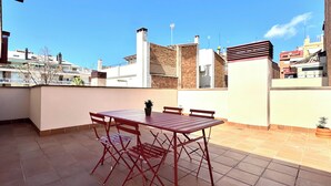 Eine Dachterrasse mit einem roten Metalltisch und -stühlen, einem Blumentopf und Blick auf umliegende Gebäude.
