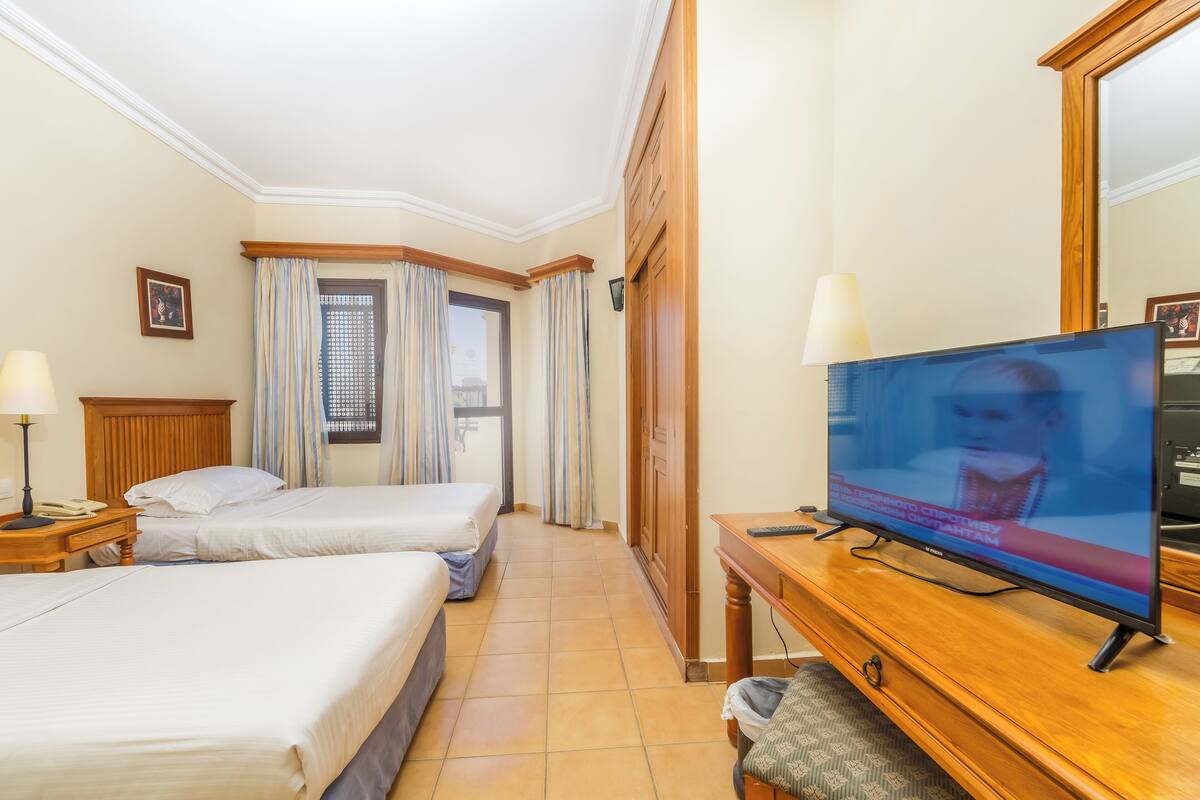 Habitación de hotel con dos camas, un aparador de madera, un televisor y una ventana con cortinas.