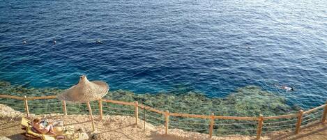 A beach with clear blue water, a wooden fence, and a straw umbrella.